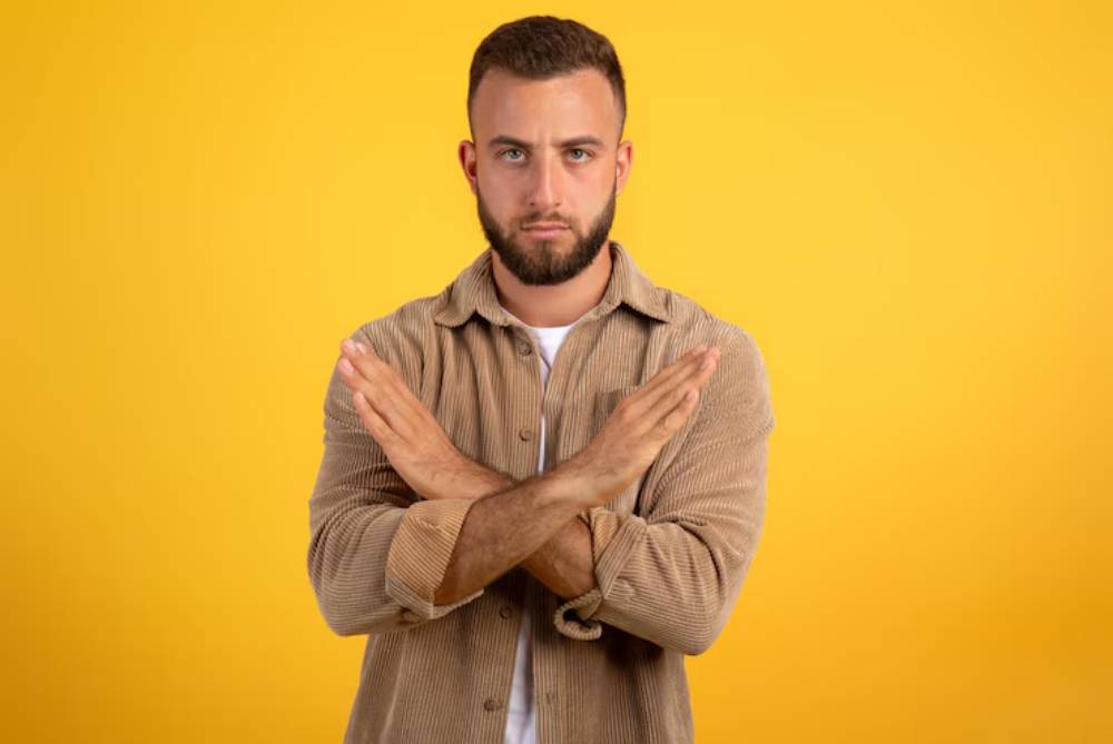 A person stands against a bright yellow backdrop, crossing their arms in a gesture of disagreement or rejection.