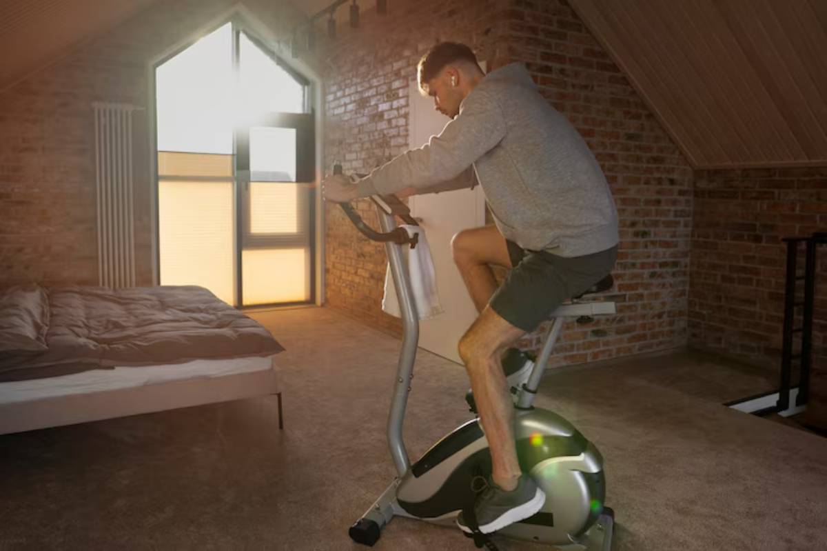 A person exercises on a stationary bike in a cozy room with brick walls and a sunlit window, creating a warm atmosphere.