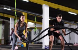 Two individuals engage in a battle rope workout in a brightly lit gym, showcasing strength and determination.