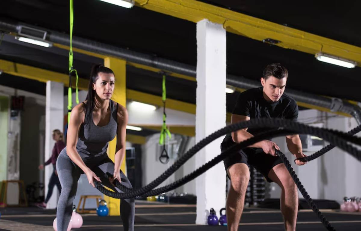 Two individuals engage in a battle rope workout in a brightly lit gym, showcasing strength and determination.