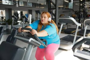 A person wearing headphones exercises on a stationary machine in a modern gym, surrounded by fitness equipment.