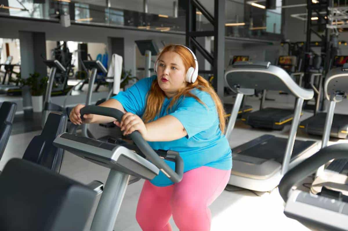 A person wearing headphones exercises on a stationary machine in a modern gym, surrounded by fitness equipment.