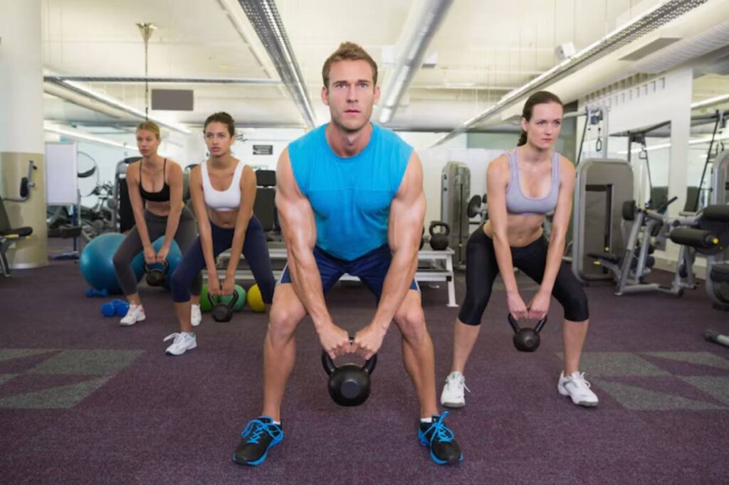 A group of four people performs kettlebell exercises in a modern gym, focusing on strength training in a vibrant setting.