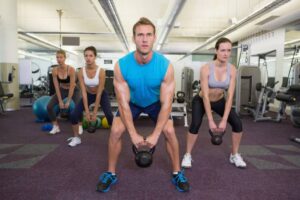 A group of four people performs kettlebell exercises in a modern gym, focusing on strength training in a vibrant setting.