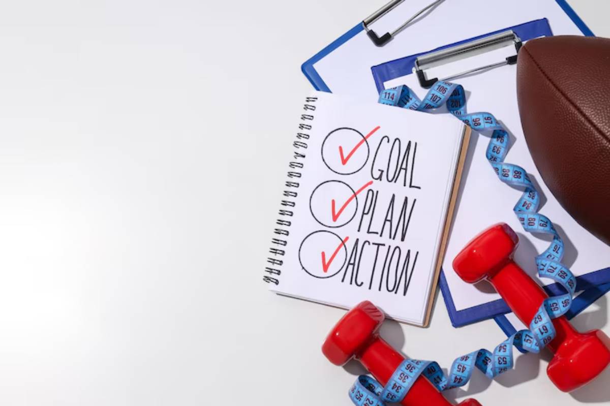 A notepad with 'GOAL,' 'PLAN,' and 'ACTION' checked off, alongside a football, dumbbells, and a measuring tape.