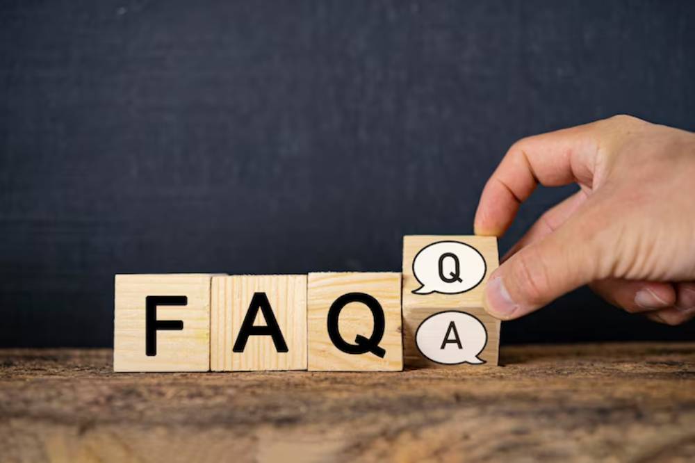 A hand places a wooden block with speech bubbles labeled 'Q' and 'A' beside the letters 'F', 'A', 'Q' on a rustic tabletop.