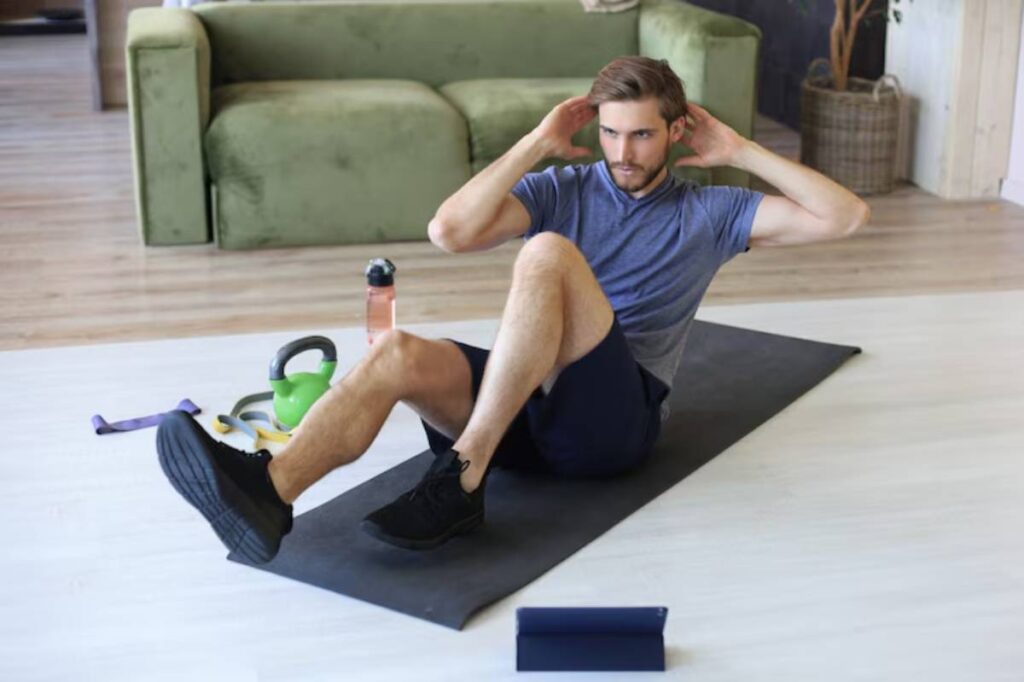 A person performs crunches on a yoga mat at home, surrounded by fitness equipment including a kettlebell and water bottle.