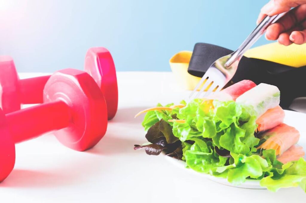 A hand holding a fork over a plate of fresh salad beside red dumbbells and fitness bands on a white table.