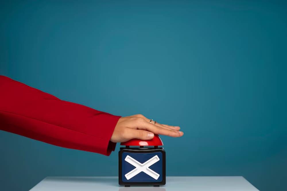 A hand is poised to press a large red button featuring a white 'X', set against a solid blue background.